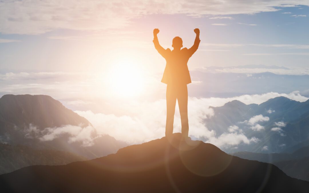 A shadow of a man standing on top of mountain after achieving success by Being Obsessed and not being just an average person.