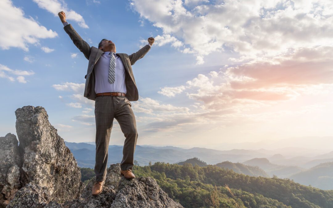 Successful businessman standing raised hand on top of peak mountain.