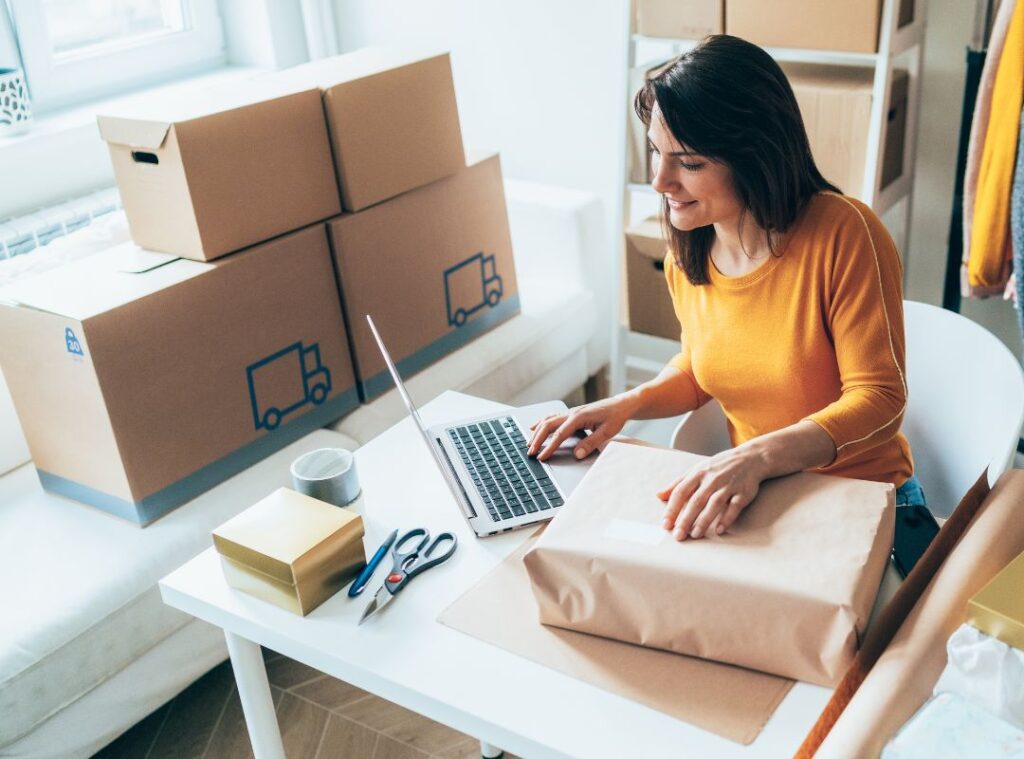 A small business owner on a laptop with a package on her side.